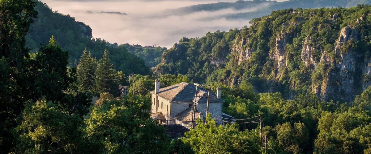 A mountain village with traditional houses nestled among lush green hills and a valley shrouded in mist.