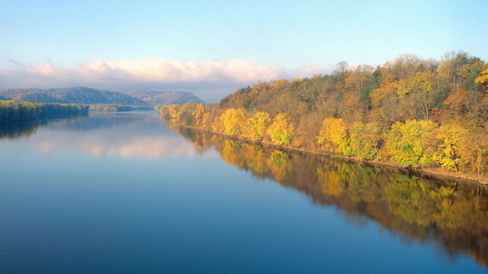 A calm river reflecting autumn foliage, surrounded by hills.