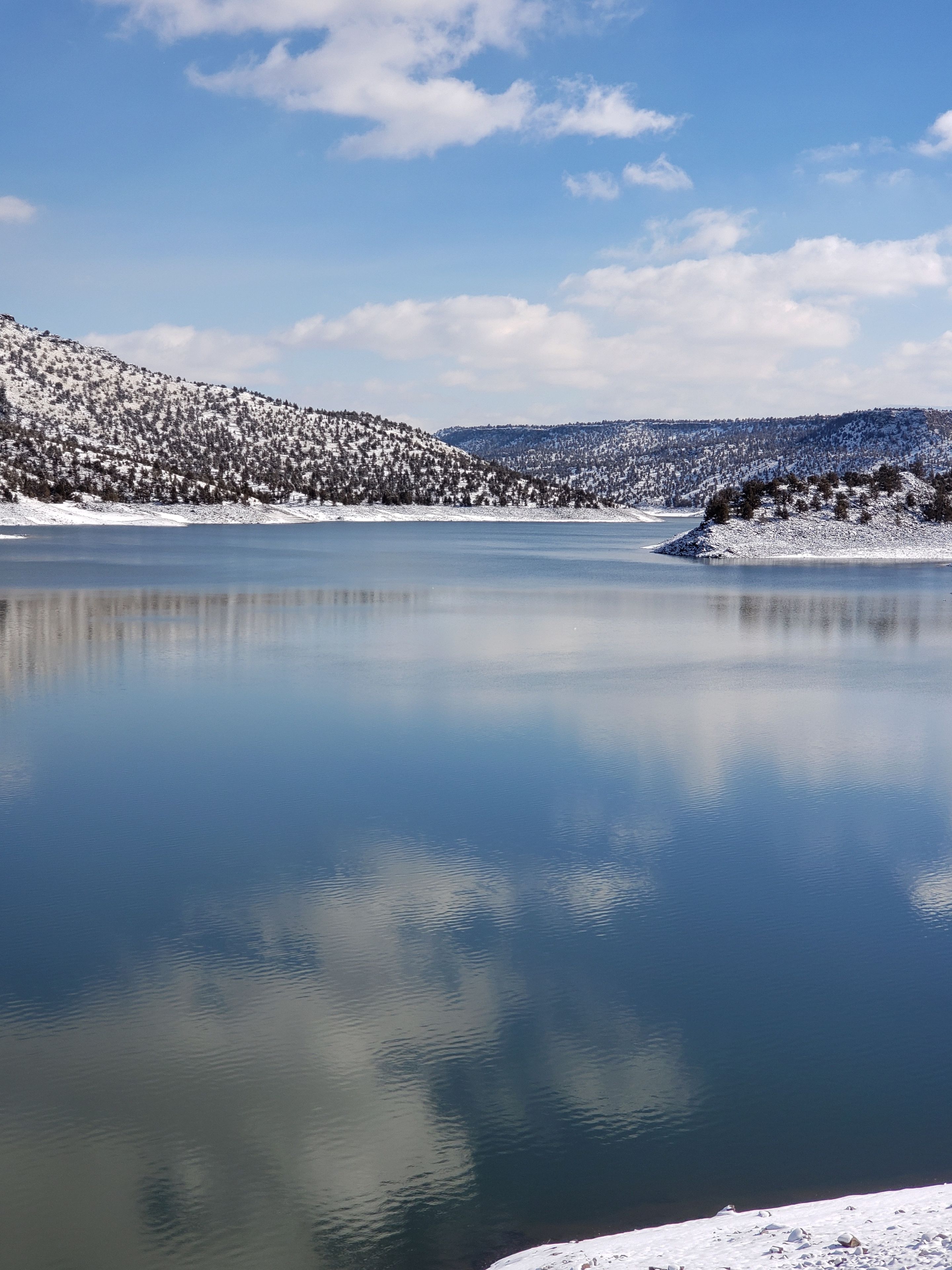 A calm lake surrounded by snow-covered hills and a clear sky.