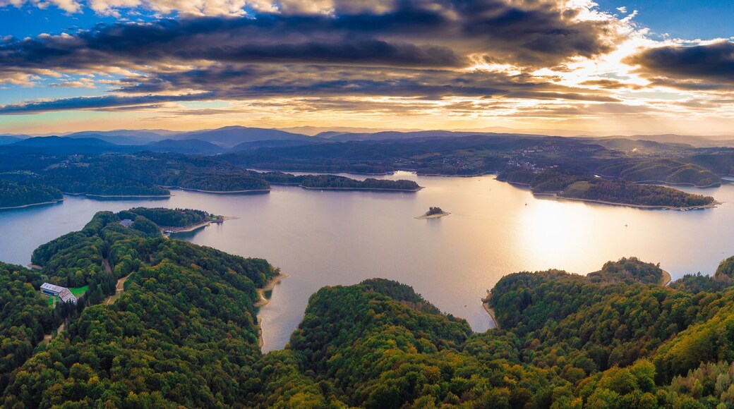 A panoramic view of a lake surrounded by forested hills and mountains.