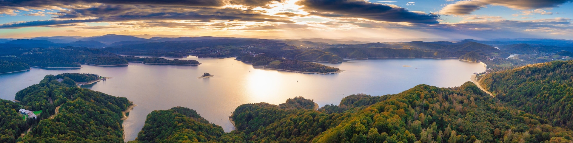 Ein weiter Blick über einen See, umgeben von bewaldeten Hügeln und Bergen.