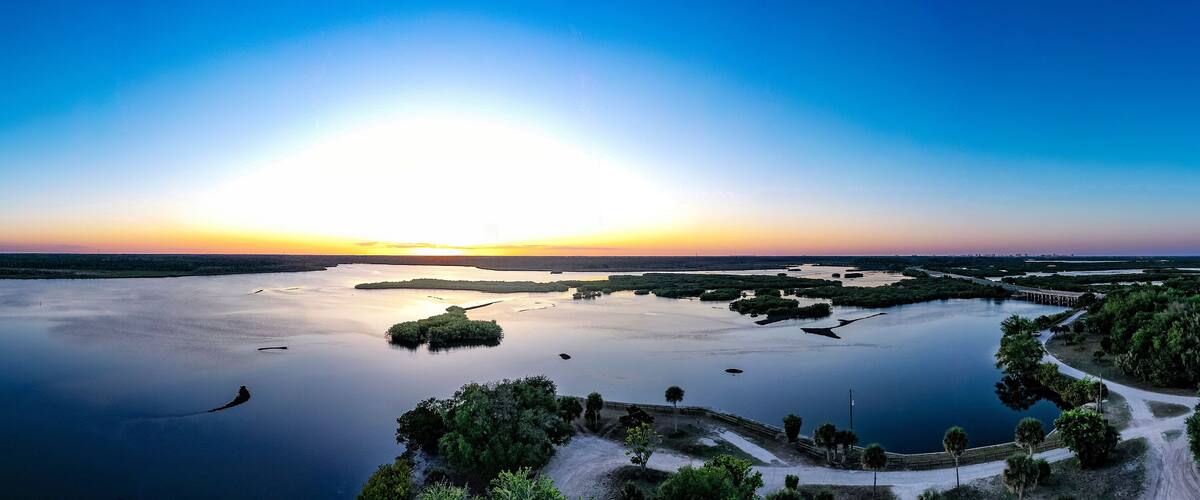 A sunset over a calm lake with islands and a bridge.