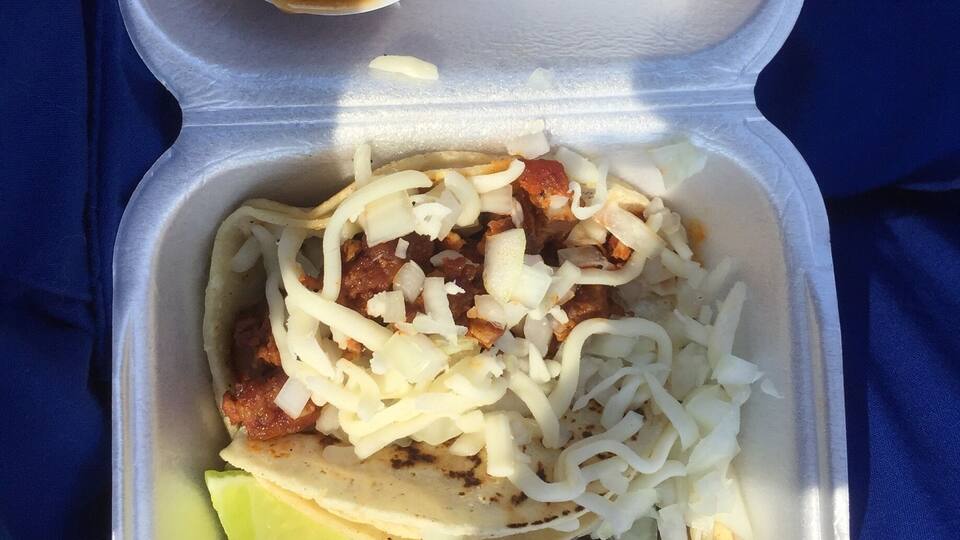 A taco with shredded cheese, meat, and a lime wedge, served with a small bowl of sauce.