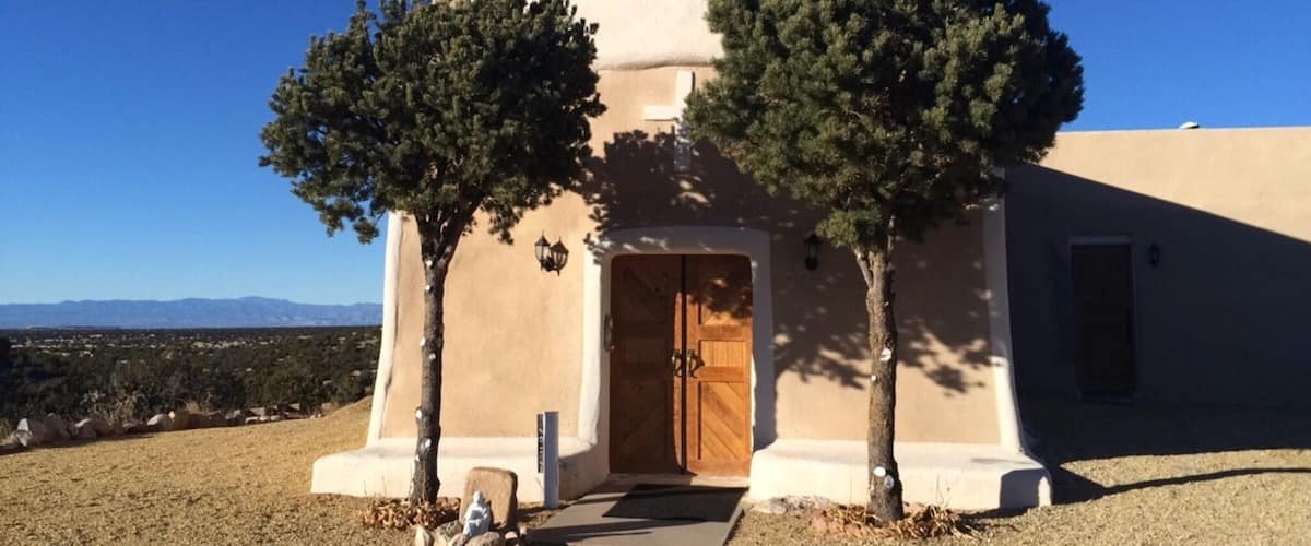 A small church with a cross on top, two trees in front, and a clear blue sky.