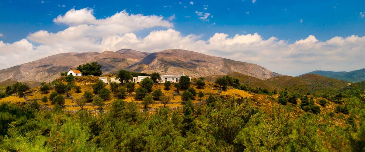 A mountainous landscape with a white building surrounded by trees and a clear blue sky.