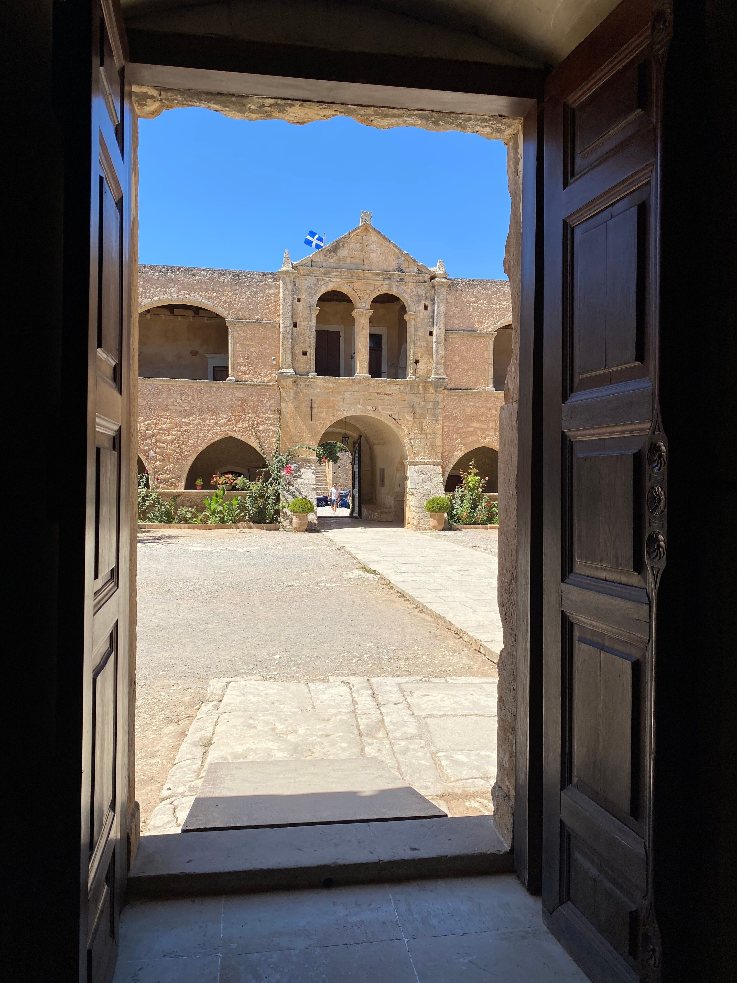A courtyard with a stone building, arched doorways, and a flag.