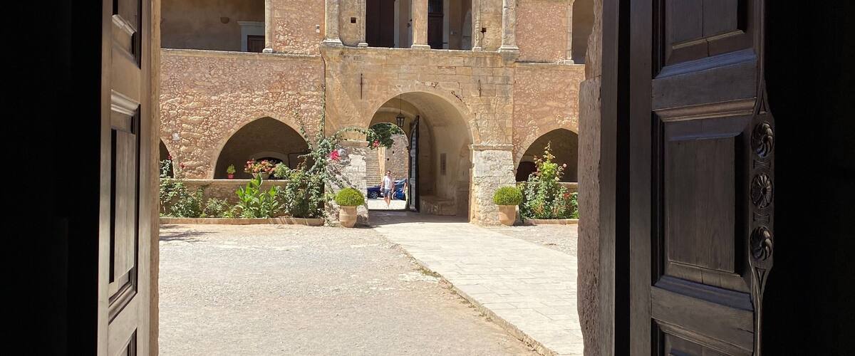 A courtyard with a stone building, arched doorways, and a flag.