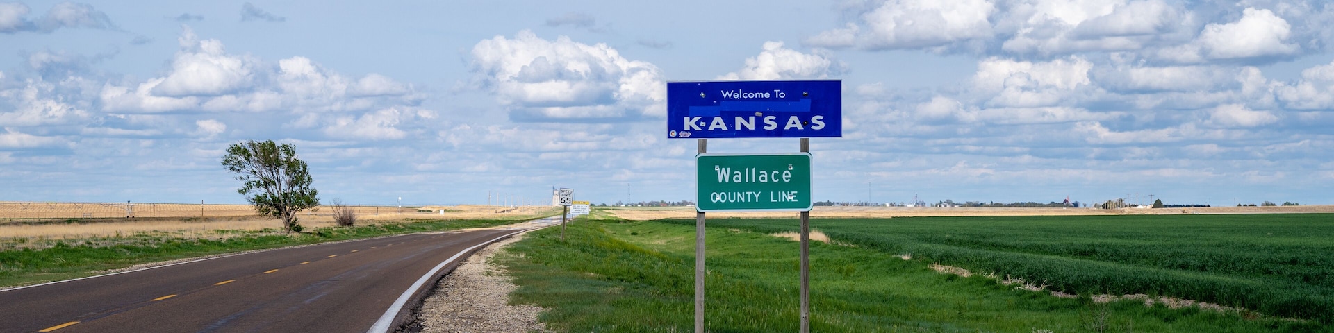 A road with a 'Welcome to Kansas' sign and a 'Wallace County Line' sign.