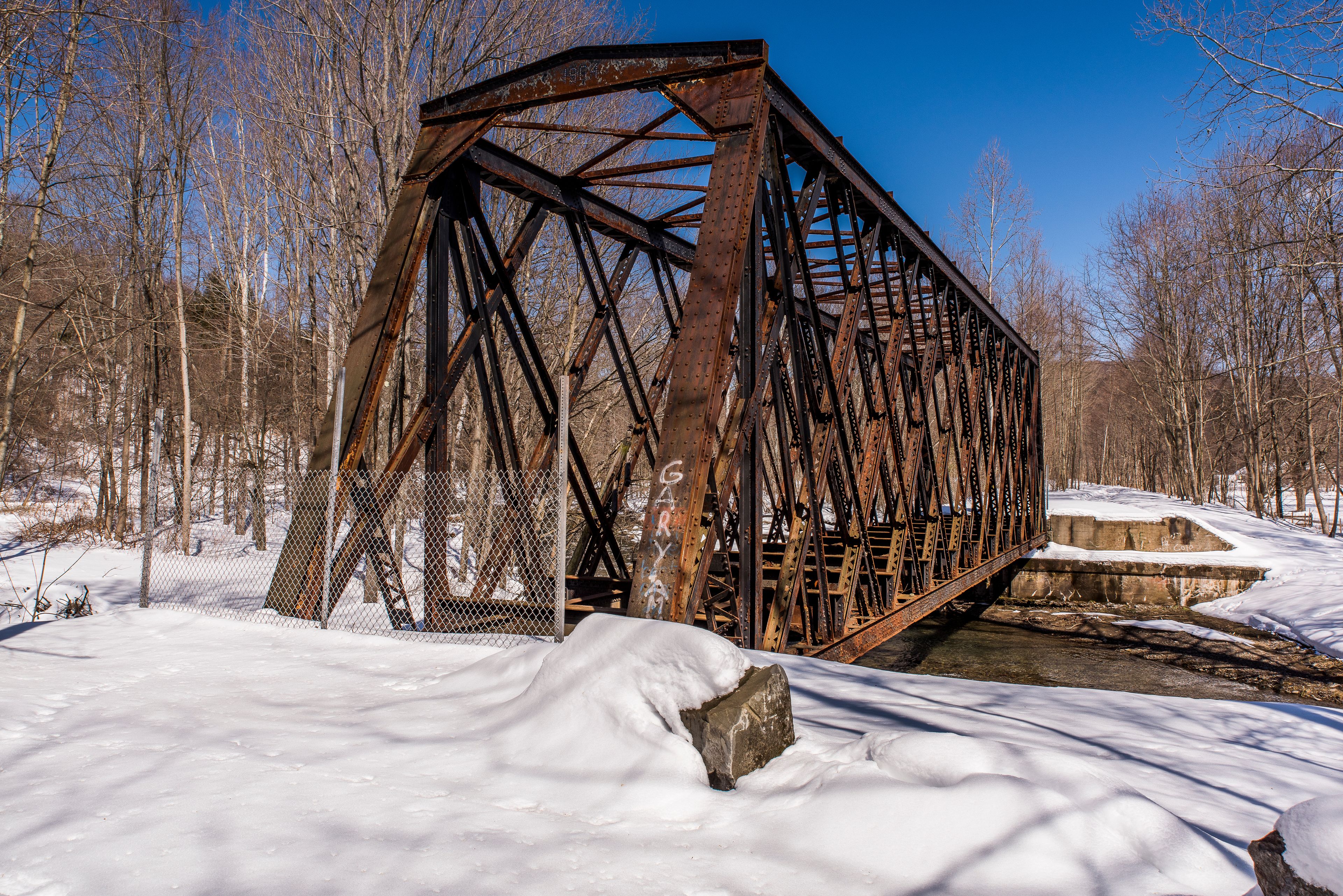 Un puente de metal oxidado en un paisaje nevado con árboles desnudos.