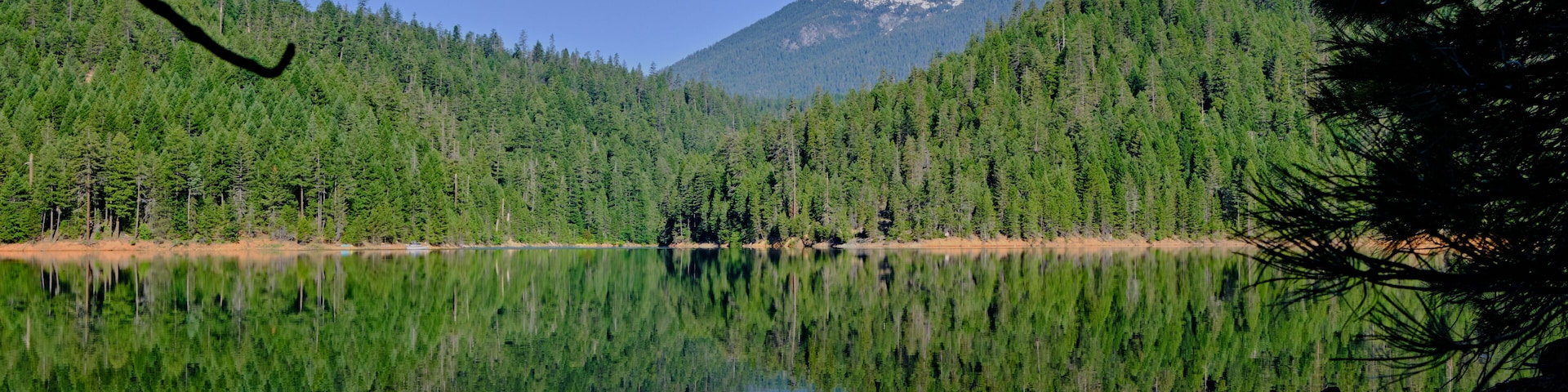 A calm lake reflecting a forested mountain range.