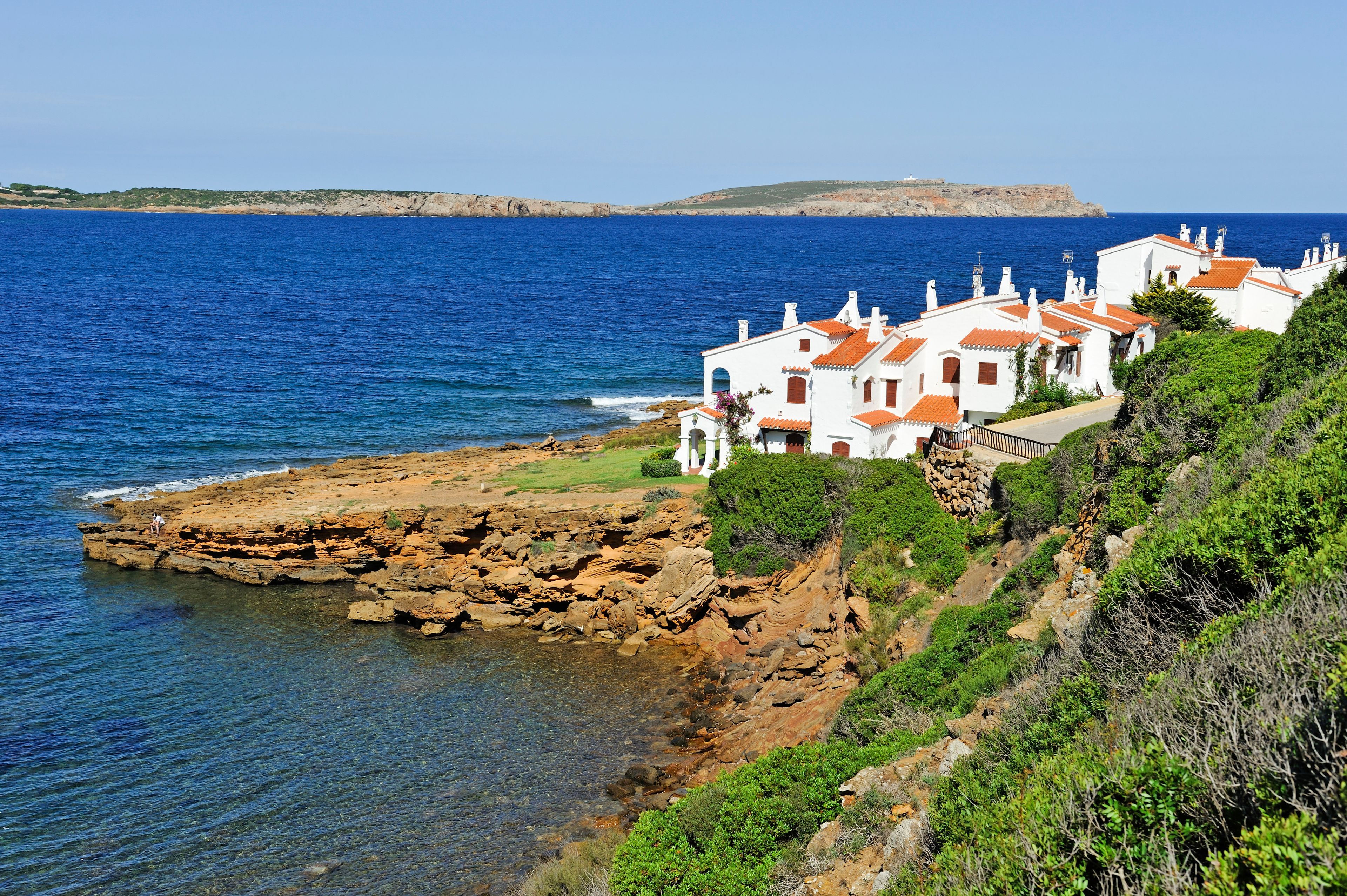 A coastal village with white buildings and red roofs, rocky cliffs, and the sea.