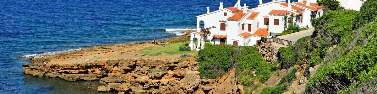 A coastal village with white buildings and red roofs, rocky cliffs, and the sea.