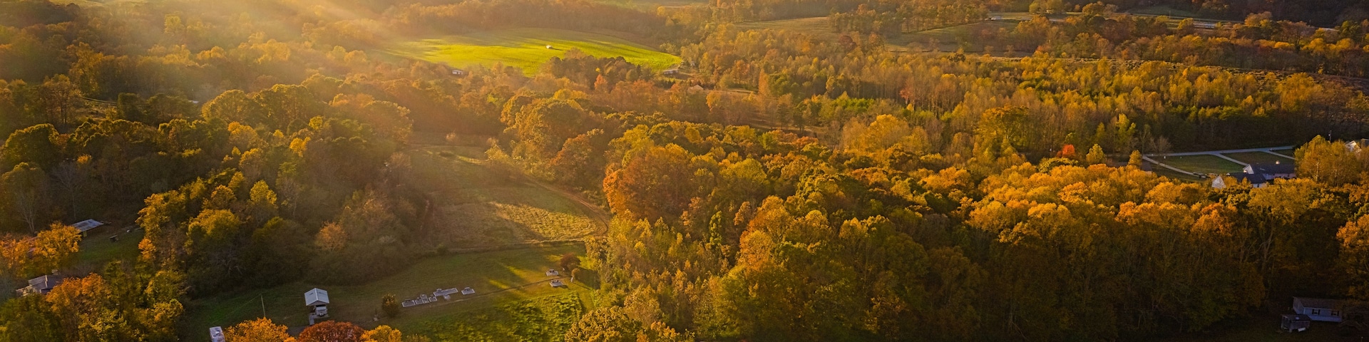 Ein weiter Blick über ein Tal mit Herbstlaub, sanften Hügeln und verstreuten Gebäuden.