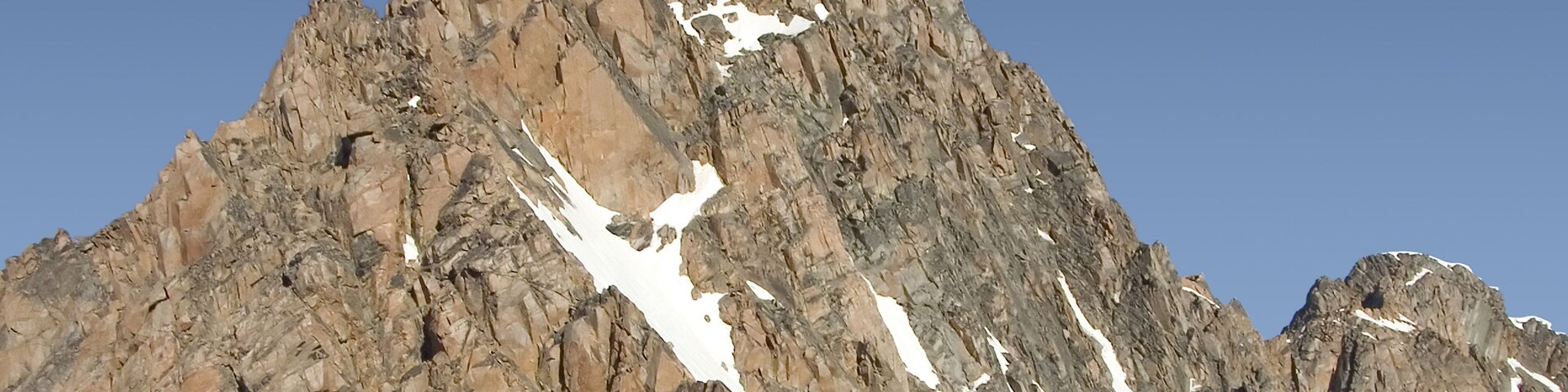 A rugged mountain peak with snow patches and clear blue sky.