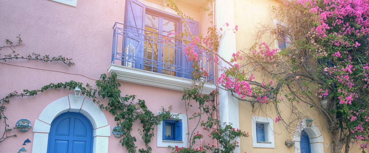 A pink and yellow building with blue doors and windows, surrounded by flowering plants and vines.