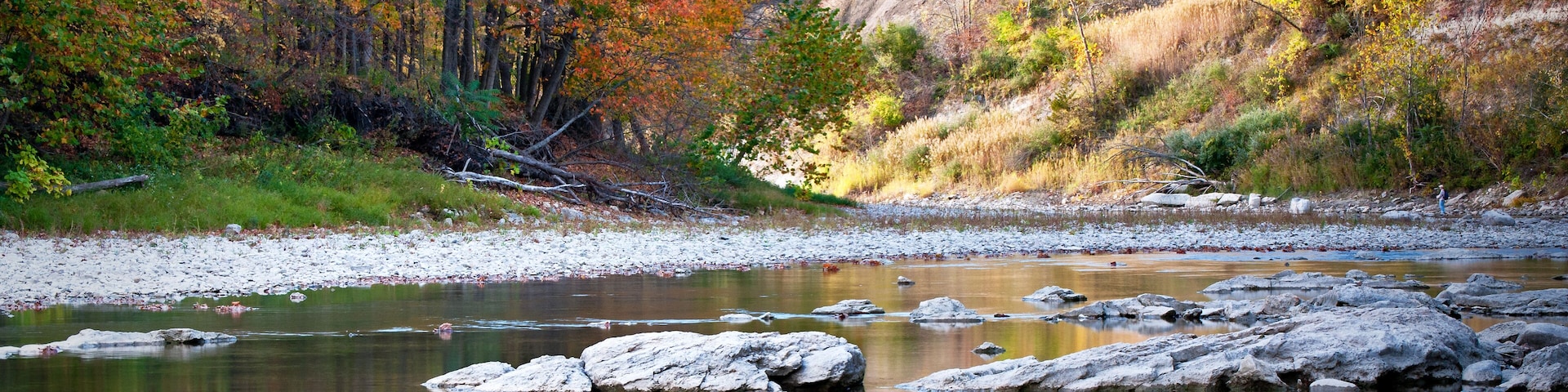 A calm river with rocks, autumn-colored trees, and a rocky cliff.