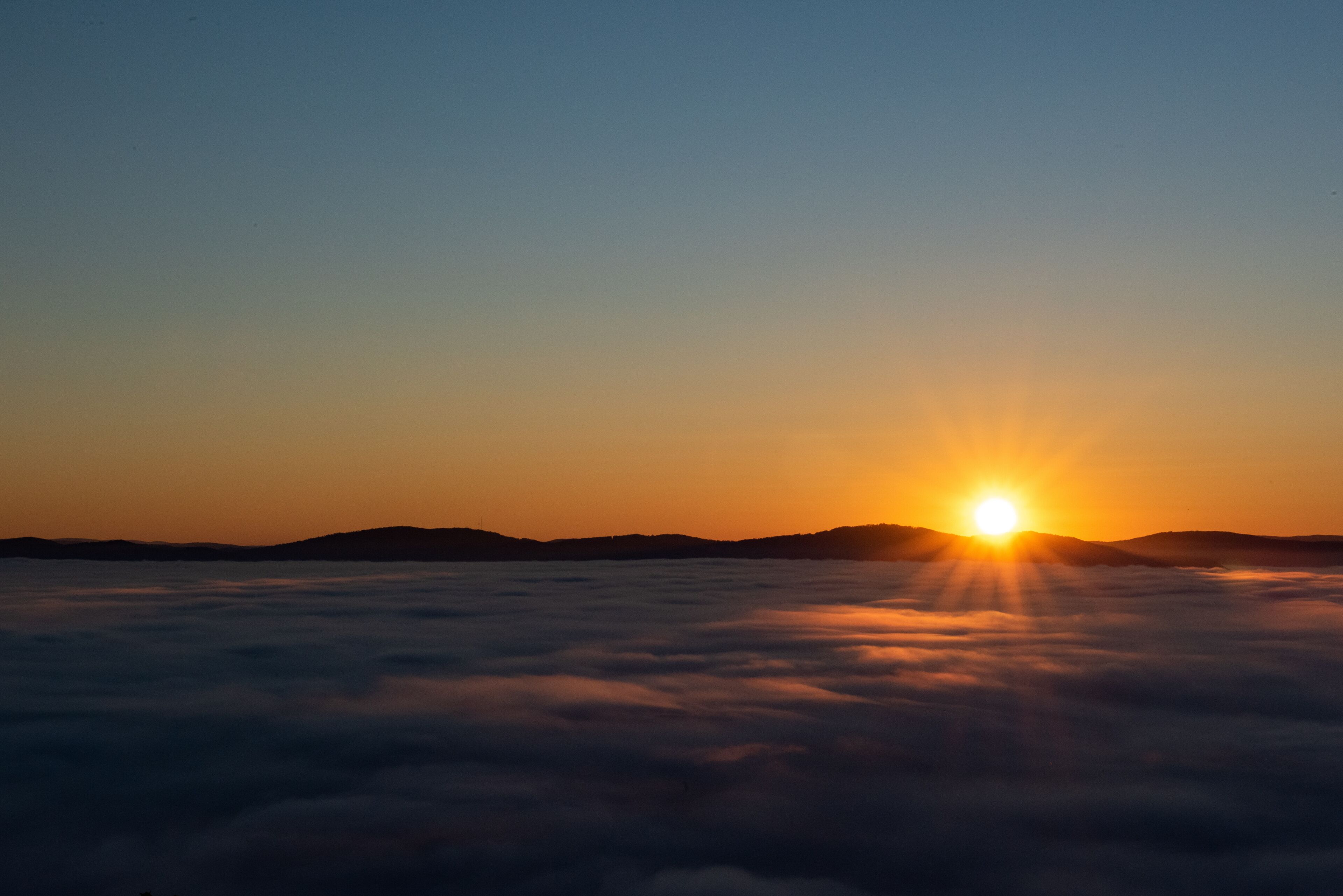 Un lever de soleil sur une mer de nuages, le soleil étant visible au-dessus de l’horizon.
