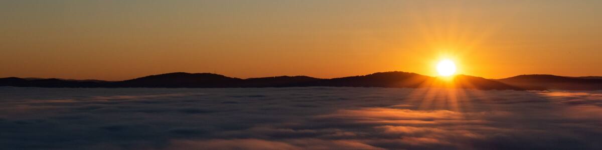 A sunrise over a sea of clouds with the sun visible above the horizon.