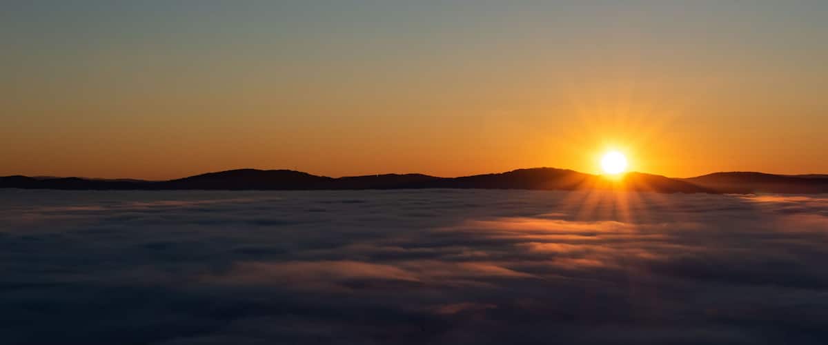 Un lever de soleil sur une mer de nuages, le soleil étant visible au-dessus de l’horizon.