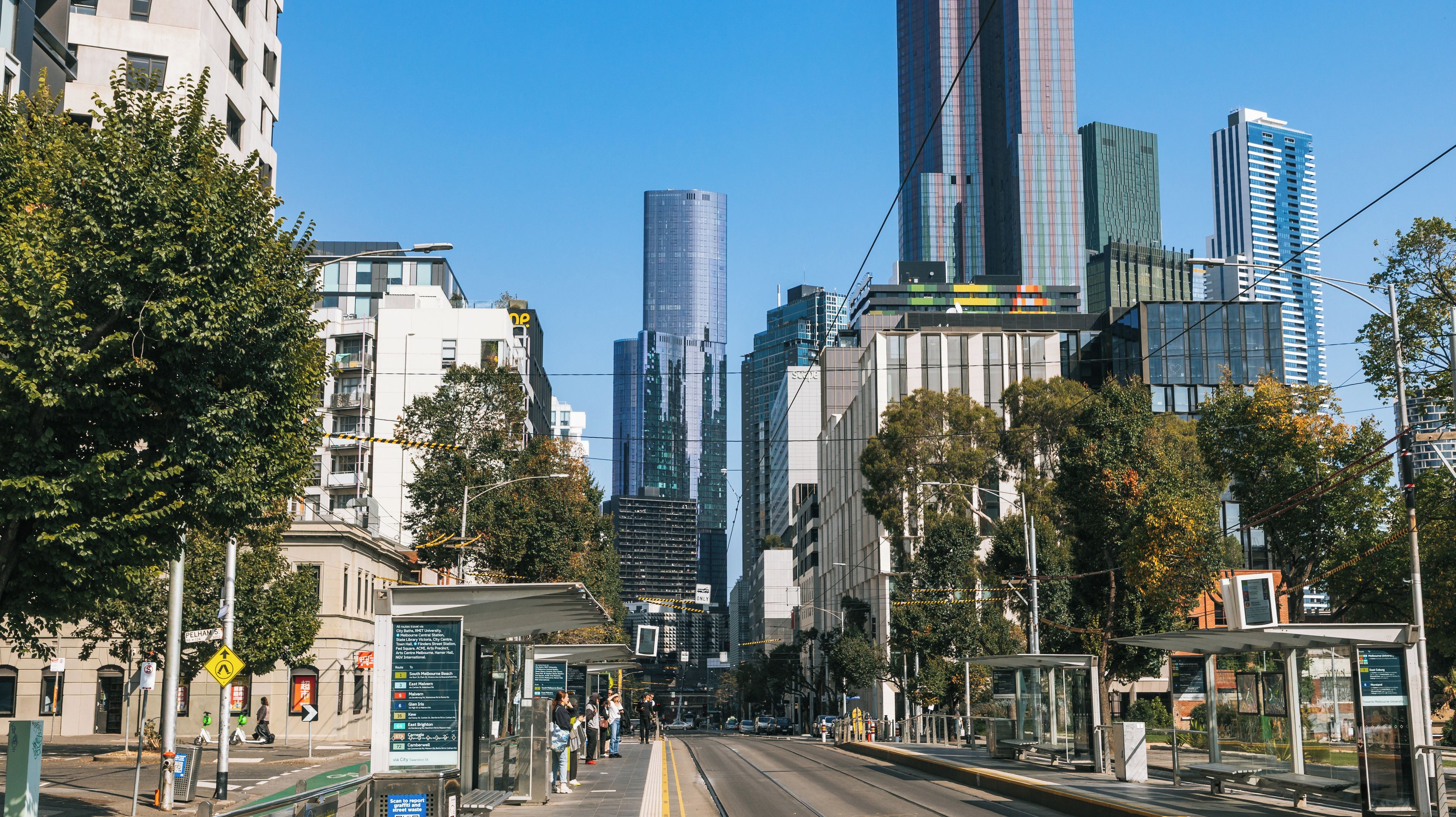 A city street lined with modern buildings, a tram, and a bus stop.