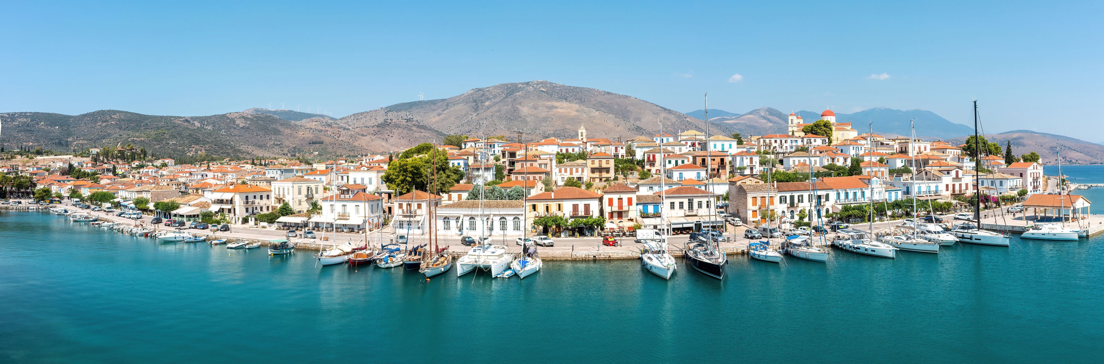 A coastal town with colorful buildings, a marina with boats, and mountains in the background.