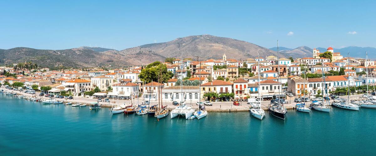 A coastal town with colorful buildings, a marina with boats, and mountains in the background.