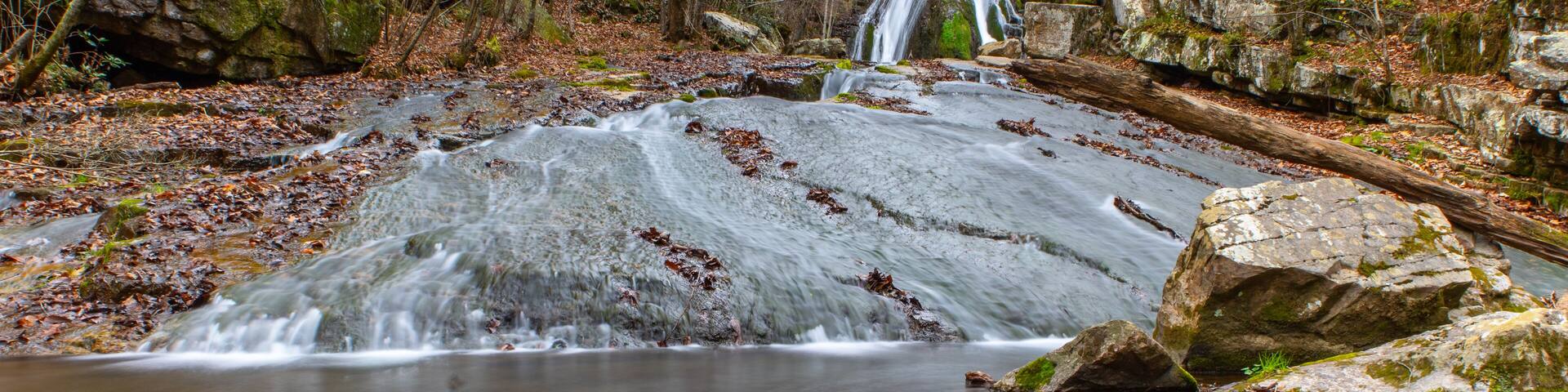 A waterfall in a forested area with a clear stream and rocks.