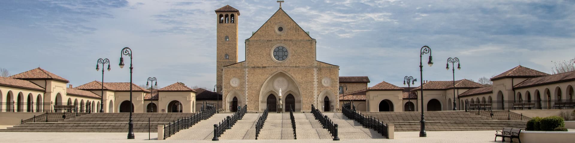A historic church with a prominent bell tower and a symmetrical facade, surrounded by a paved square with steps leading to the entrance.