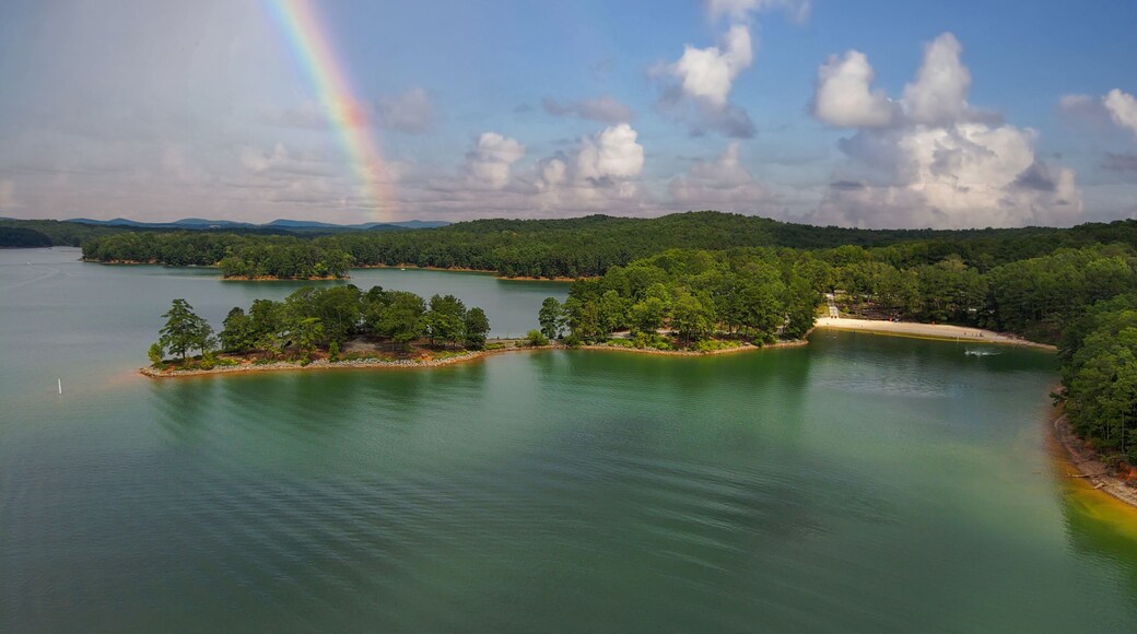 an aerial shot of a gorgeous summer landscape on the lake with rippling green water surrounded by lush green trees, grass and plants with blue sky, clouds and a rainbow at Red Top Mountain State Park
