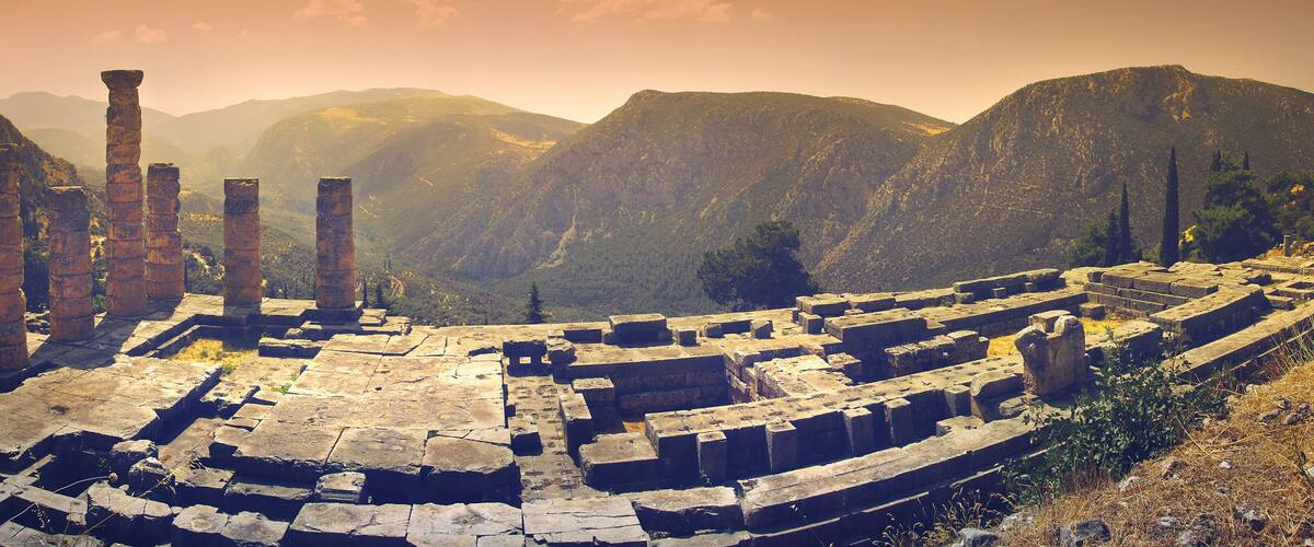 Ancient ruins with stone columns and stepped structures in a mountainous landscape.