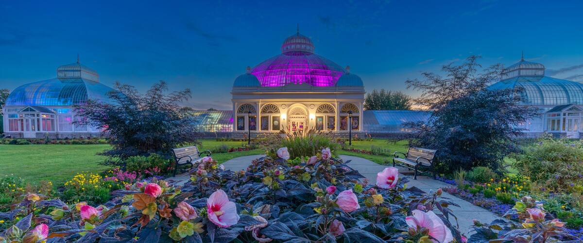 A conservatory with a glass dome, surrounded by a garden with pink flowers and benches.