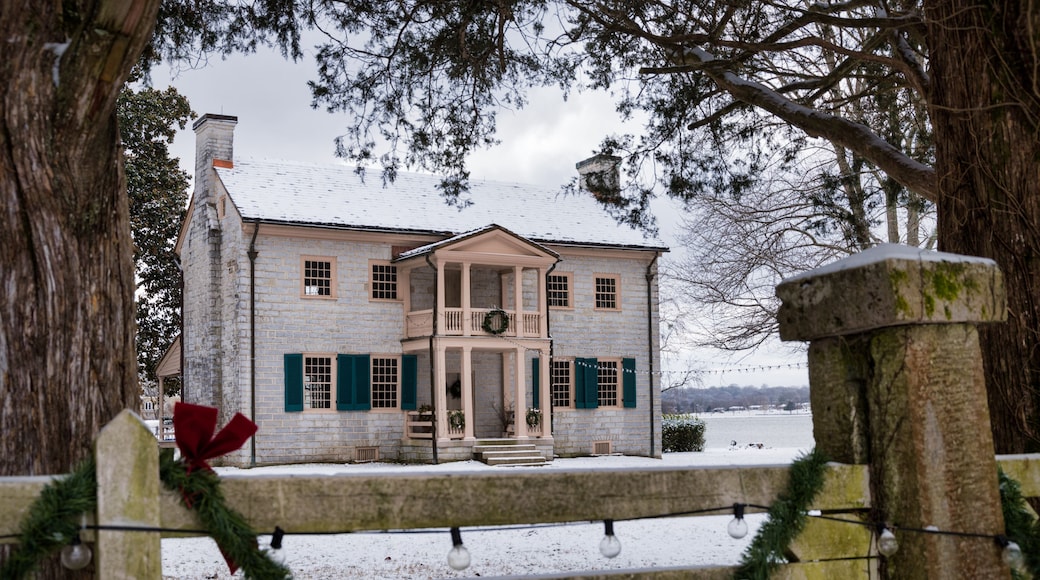 Une maison recouverte de neige, avec un porche, une clÎture en bois et une couronne de Noël.