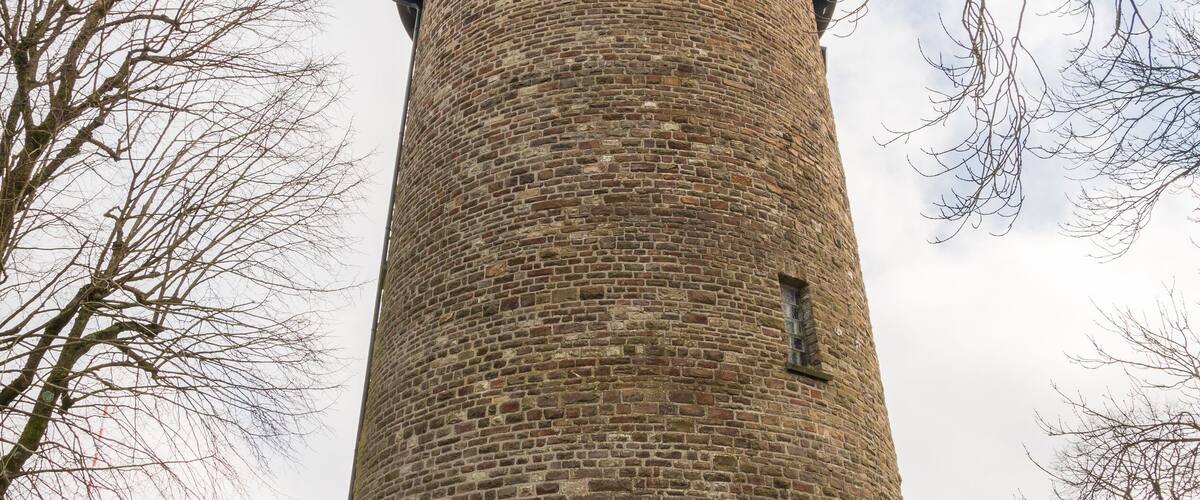A tall brick tower with a cylindrical shape and a conical roof.