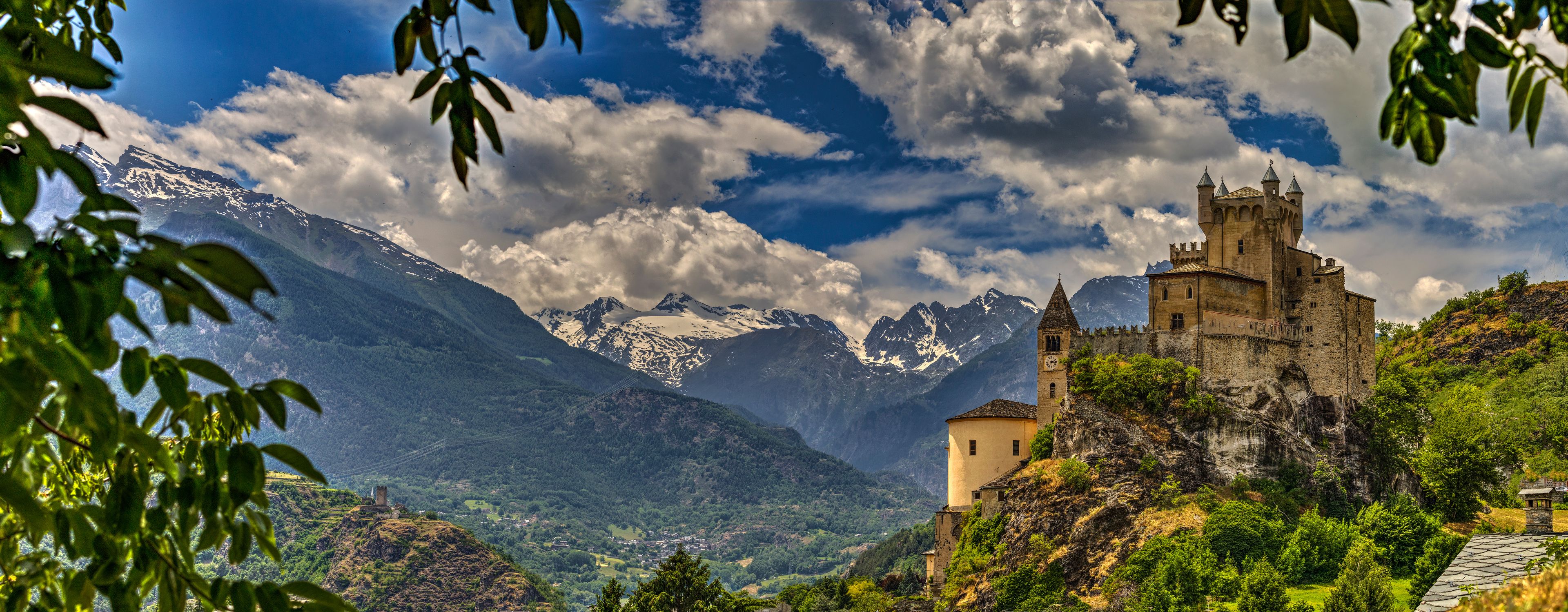 A castle on a hill with snow-capped mountains in the background.