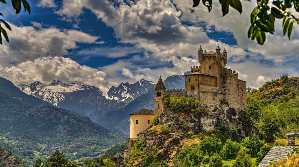 Un castillo en una colina con montañas nevadas al fondo.