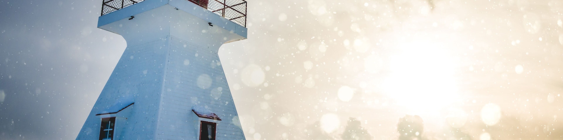 A white lighthouse with a red top, surrounded by snow.