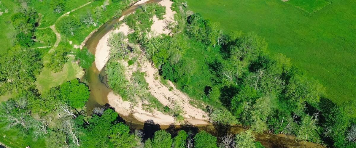 Panorama aerial view sandy river bank Lick Fork Gasconade River running water moving to lower level in Wright County, Mansfield, Missouri, large grassy meadow vacant farmland, rural countryside