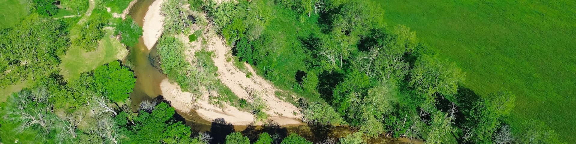 Panorama aerial view sandy river bank Lick Fork Gasconade River running water moving to lower level in Wright County, Mansfield, Missouri, large grassy meadow vacant farmland, rural countryside