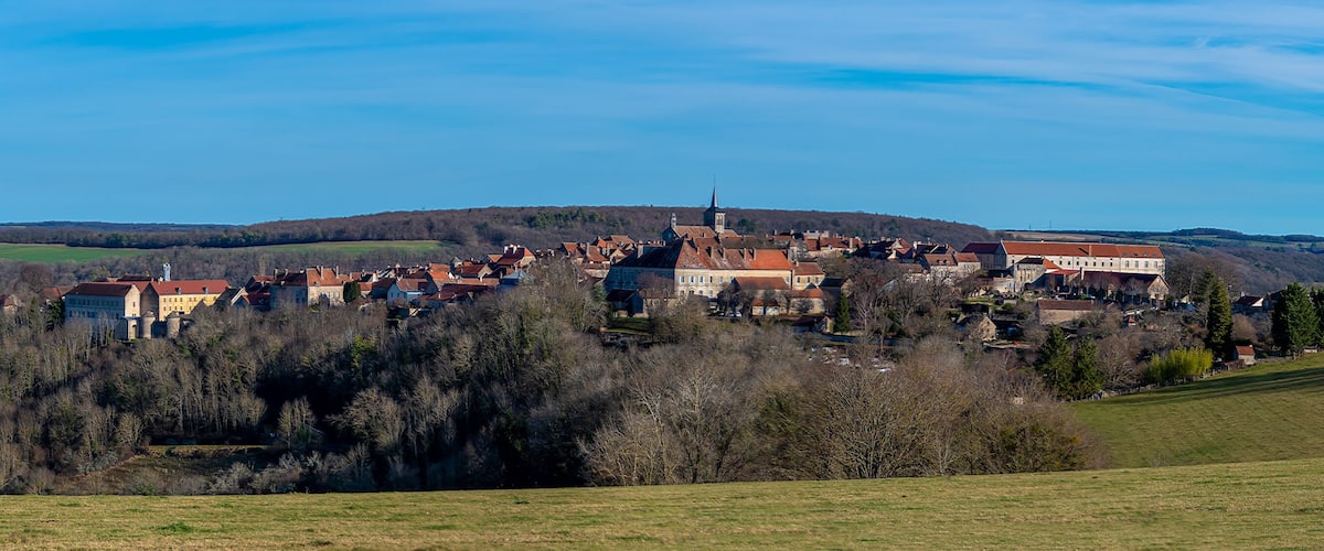 A town with historic buildings on a hill, surrounded by fields and trees.
