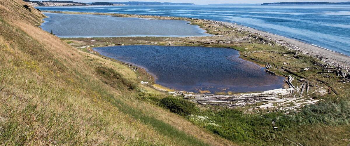 Un paysage côtier avec trois grands étangs, des collines verdoyantes et une ligne de côte lointaine.