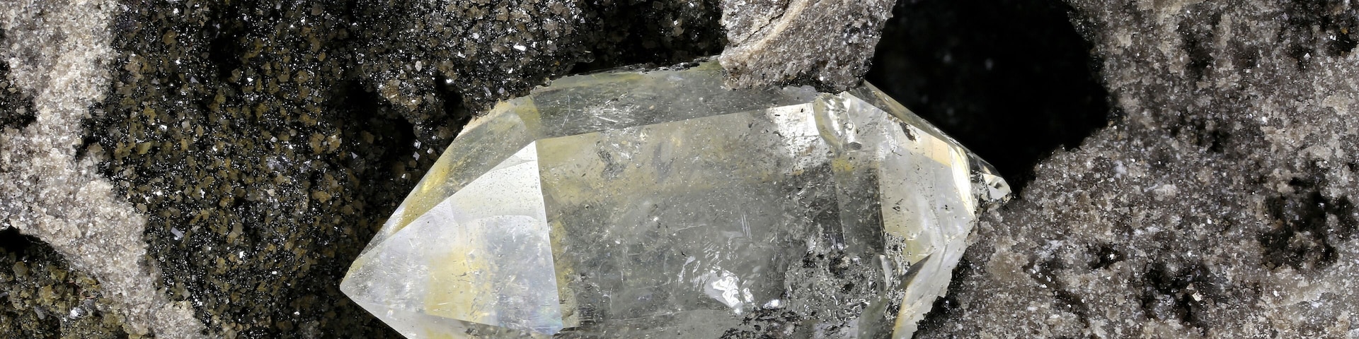 Cristal mineral translúcido incrustado em uma superfície rochosa irregular.