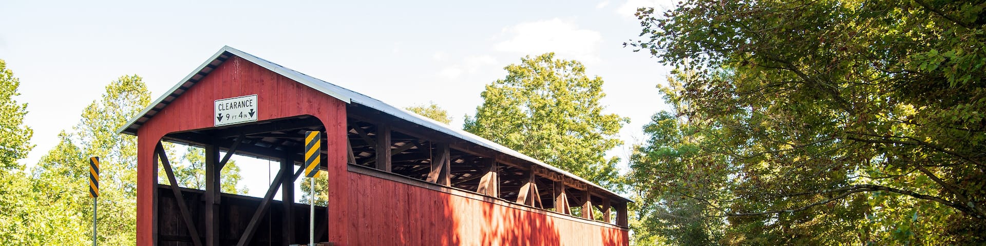A red covered bridge with a clearance sign, surrounded by lush greenery and trees.