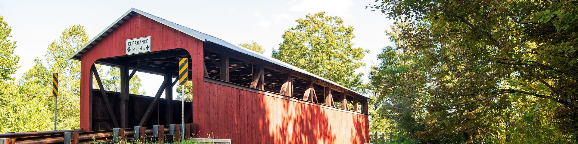 A red covered bridge with a clearance sign, surrounded by lush greenery and trees.