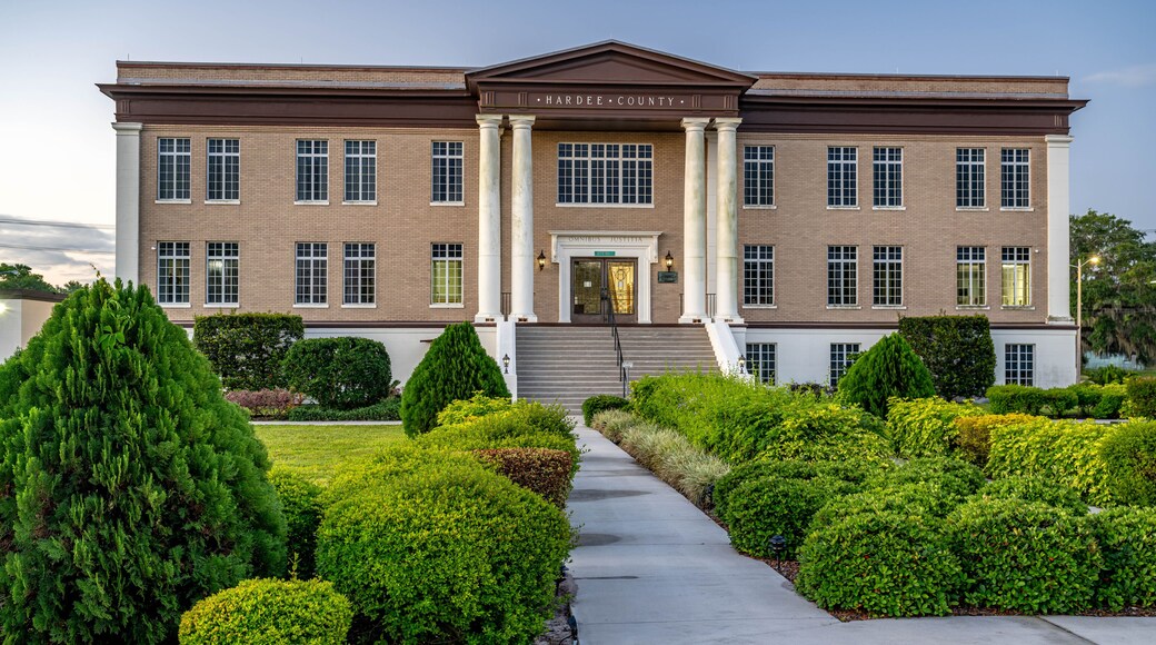 A brick courthouse with columns, a central entrance, and a well-maintained garden with various shrubs.
