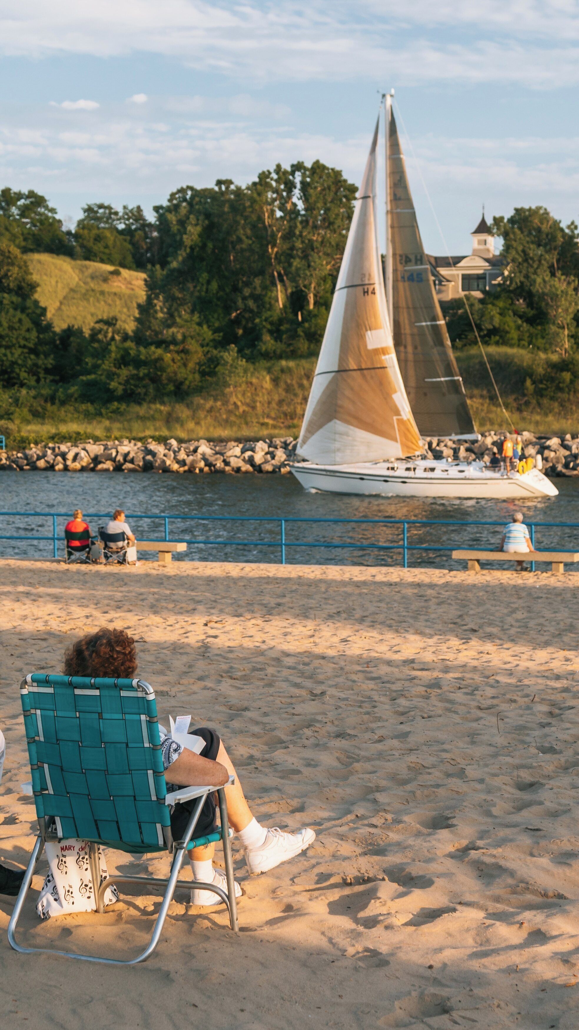 Relaxing by the shore while sailboats glide through the calm waters of Holland State Park in Michigan during a warm summer evening