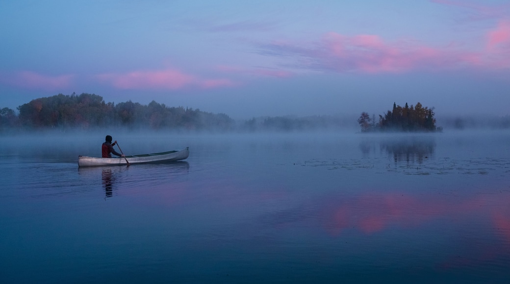 A calm lake with a person paddling a canoe, surrounded by mist and trees.