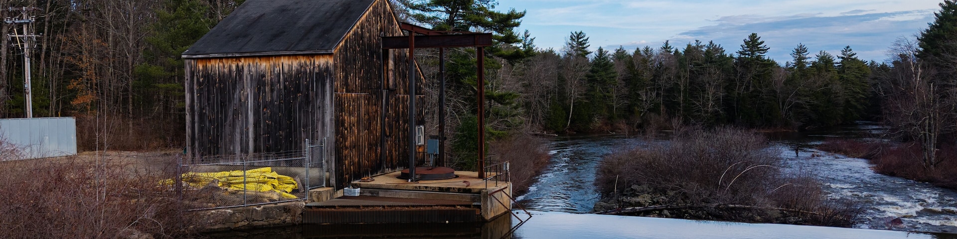 Une construction rustique en bois, située au bord d’une rivière paisible et entourée d’une forêt dense.