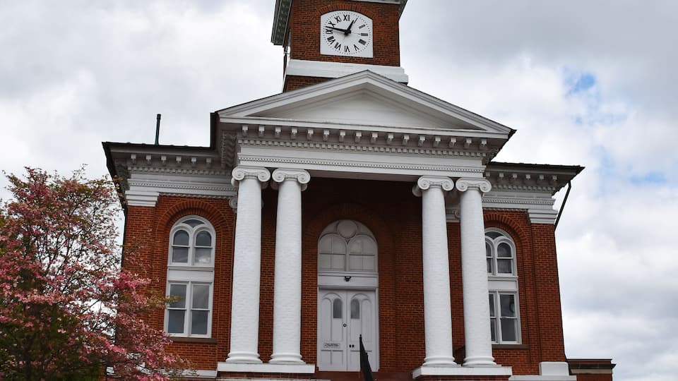 A red brick church with a clock tower, white columns, and a rose bush in front.
