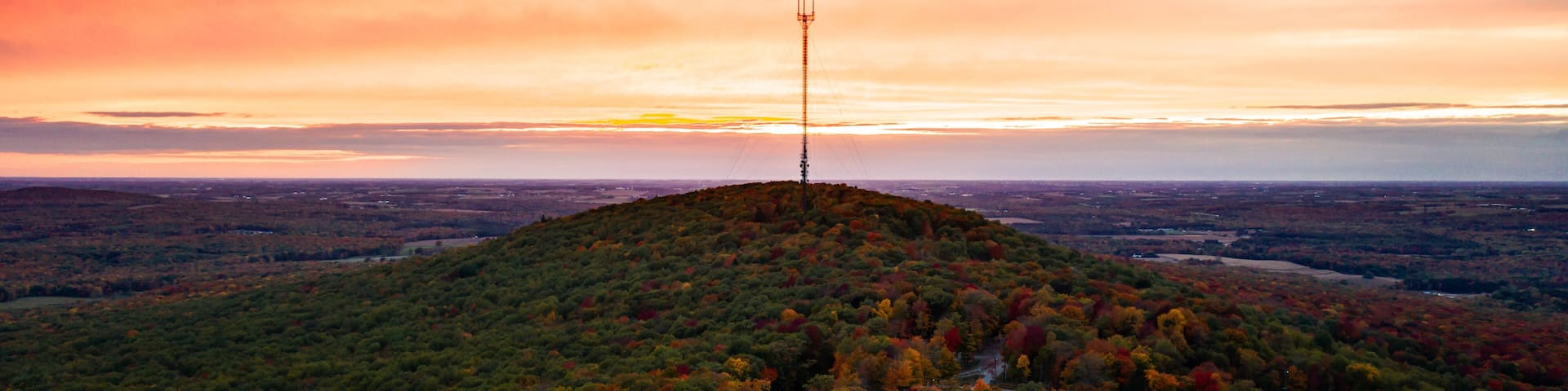 A hilltop with a communication tower, surrounded by autumn-colored trees and a winding road.