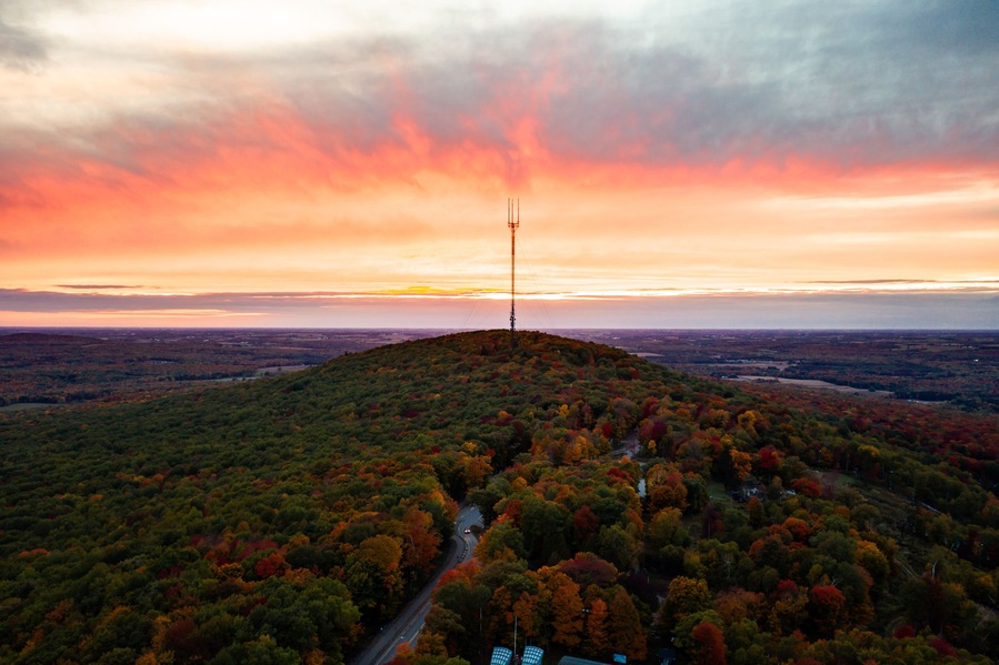 A hilltop with a communication tower, surrounded by autumn-colored trees and a winding road.